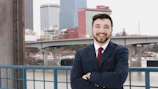 A smiling worker holding a contract with a city skyline in the background.