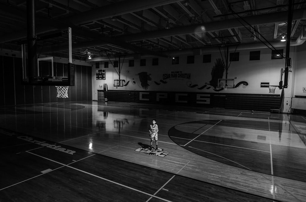 バスケットボールコートに立っているボールを保持している少年のグレースケール写真