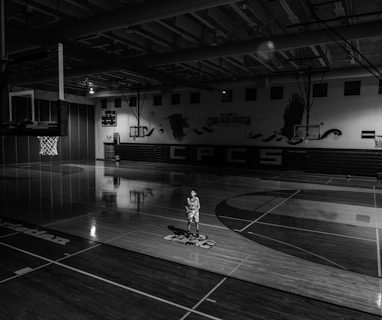 grayscale photo of boy holding ball standing on basketball court