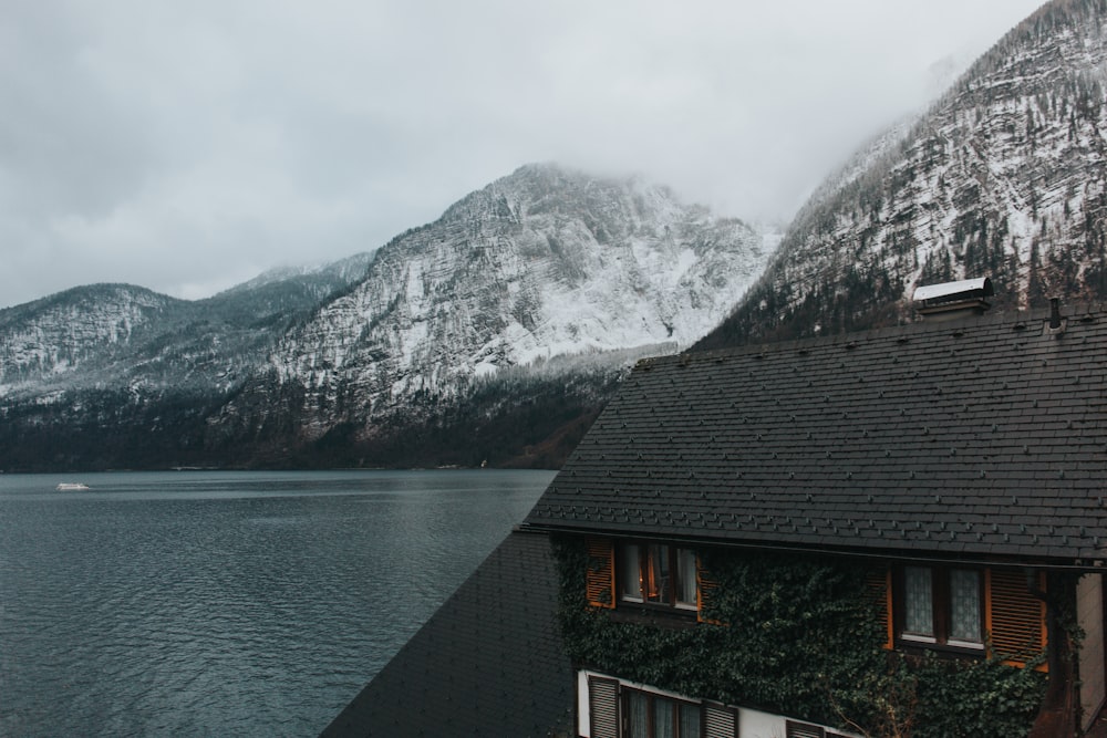 black and brown painted 2-story house near body of water and gray mountains covered with snow during daytime