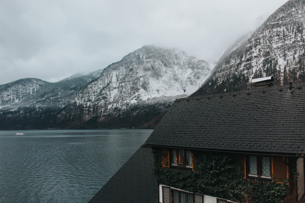 日中は雪に覆われた水域と灰色の山々の近くにある黒と茶色に塗られた2階建ての家