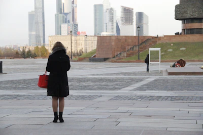 A stylish leather bag hanging from a modern city bench with blurred skyscrapers behind.