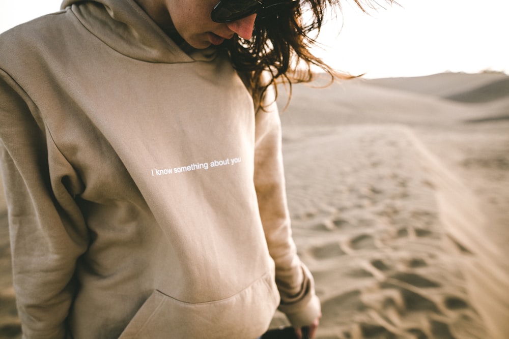 Person mit Sonnenbrille und Kapuzenpullover auf Sand