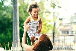 selective focus photo of woman lifting child during daytime