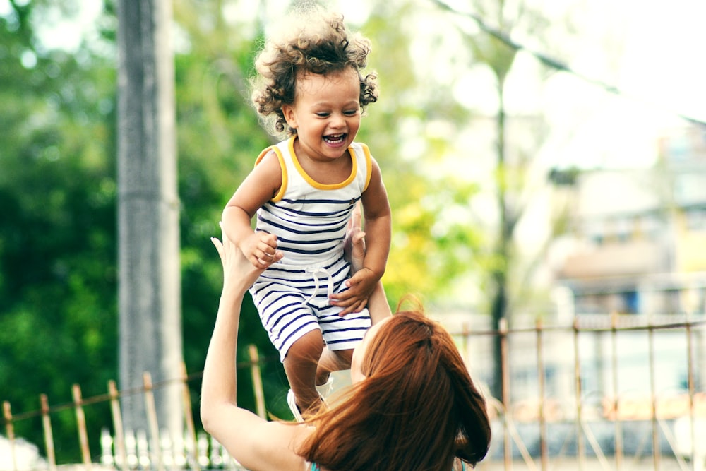 selective focus photo of woman lifting child during daytime
