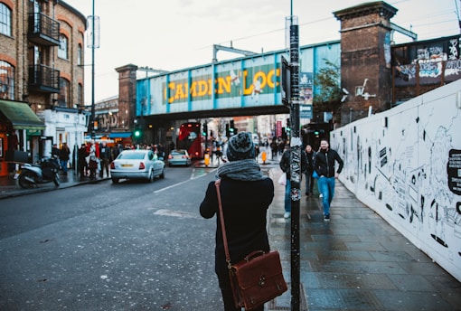 people walking on black concrete road beside buildings under white sky during daytime