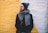 man in black coat with grey scarf standing on front of white and yellow painted wall