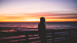 Sunset silhouette of a woman standing on a pier wearing elegant myvenus sandals, the sky painted in warm hues.
