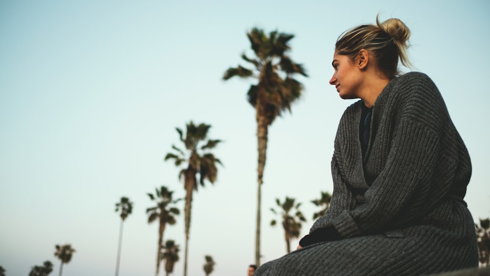 woman wearing gray sweater sitting with the distance of coconut trees under white cloudy sky