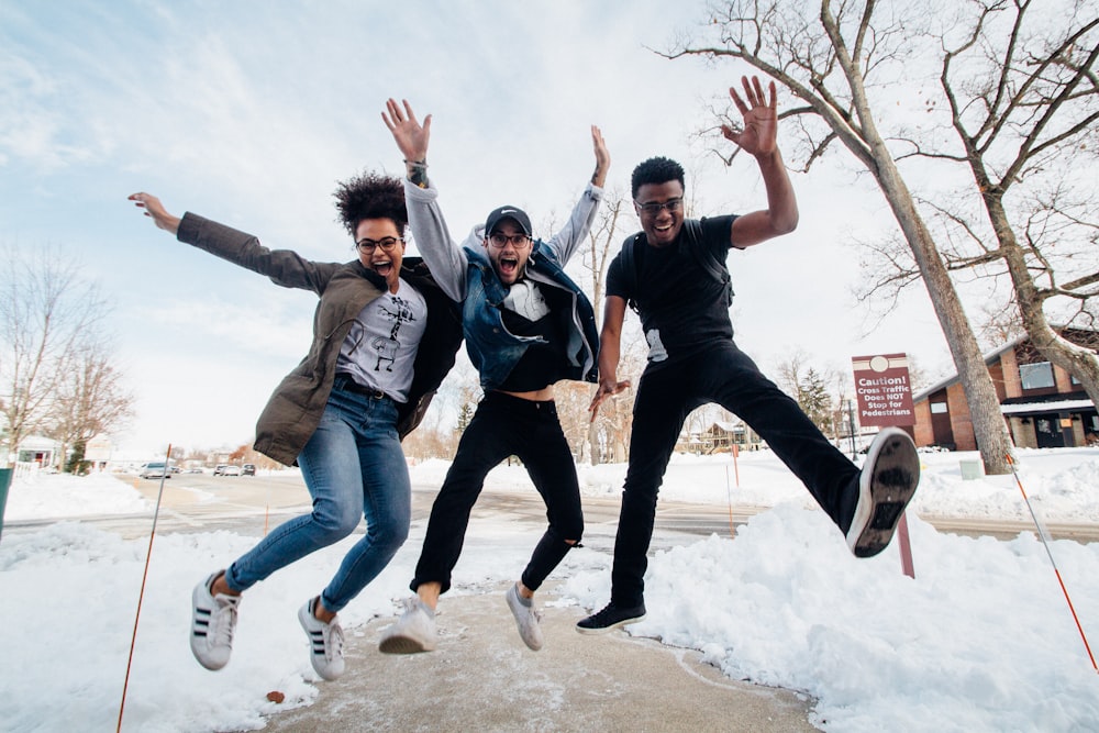 photo of three men jumping on ground near bare trees during daytime