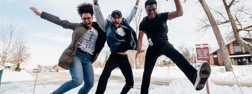 photo of three men jumping on ground near bare trees during daytime