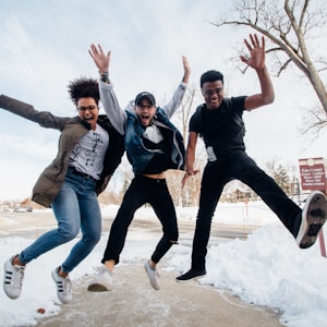 photo of three men jumping on ground near bare trees during daytime