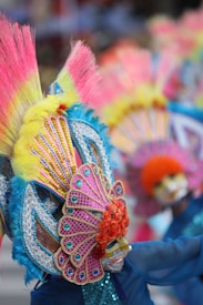 Colorful and extravagant costumes with intricate designs featuring large headdresses adorned with vibrant feathers and beads. The scene is lively and festive, showcasing cultural celebration and artistic craftsmanship.