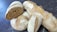 Several loaves of artisanal bread are scattered on a dark surface. The bread has a rustic appearance with a coated flour crust and varying shades of brown. One loaf is sliced open, revealing a dense, textured crumb.
