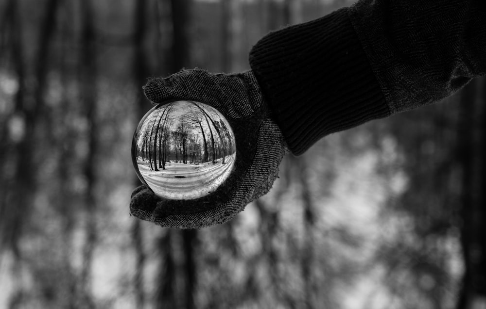 persona che tiene la fotografia in scala di grigi della sfera di cristallo chiara