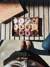 A delivery person carrying a box of colorful assorted donuts in a tropical setting.