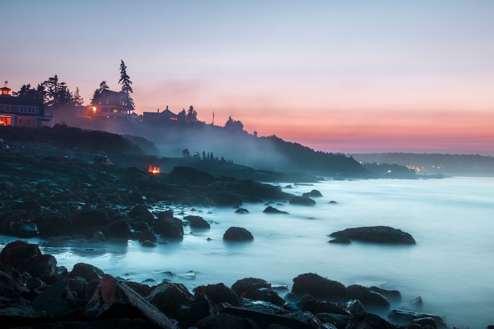 Sunset on a rocky coastline of Ogunquit where groups of people are watching an ocean mist rising from the waters