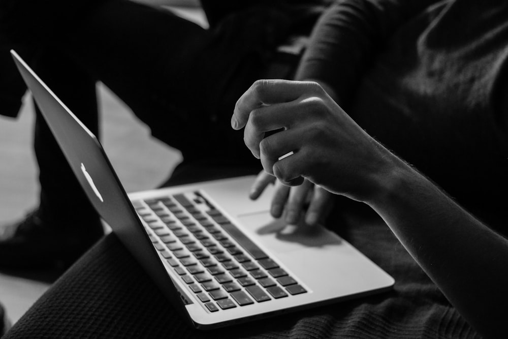 A black-and-white shot of a person working with a MacBook on their lap