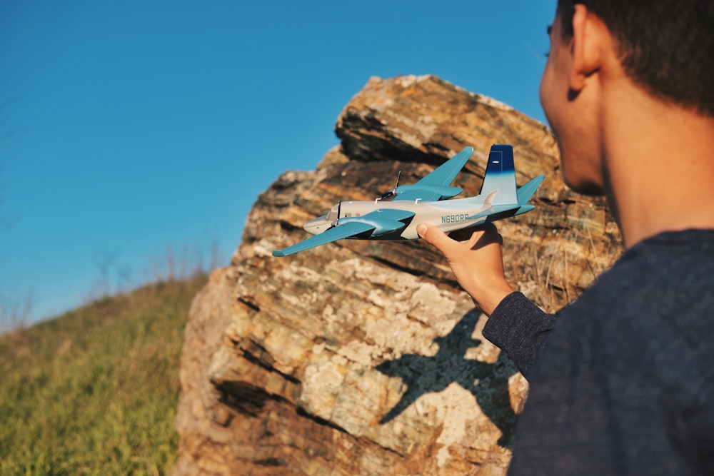 person holding blue airliner beside rock