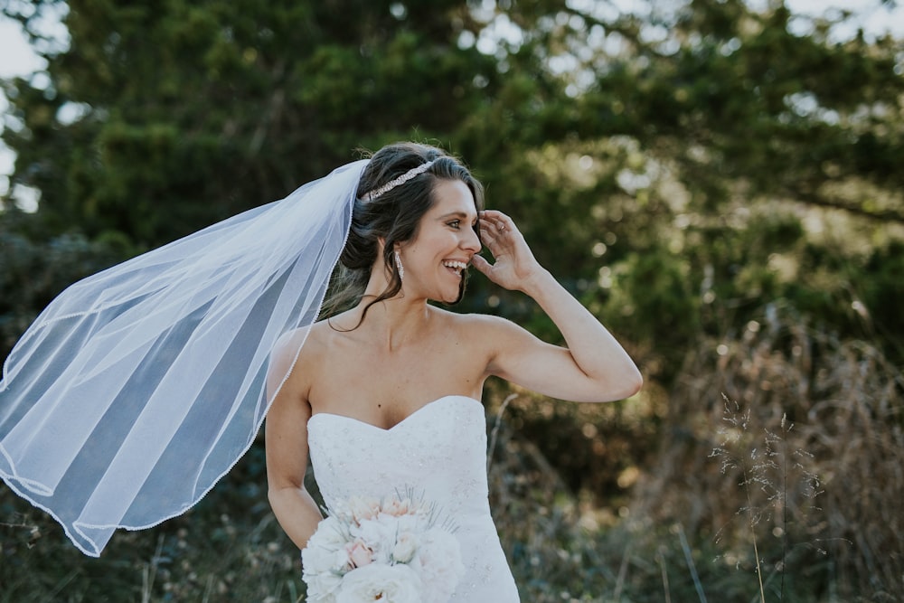 Bride stands in front of trees laughing as the wind blows her veil