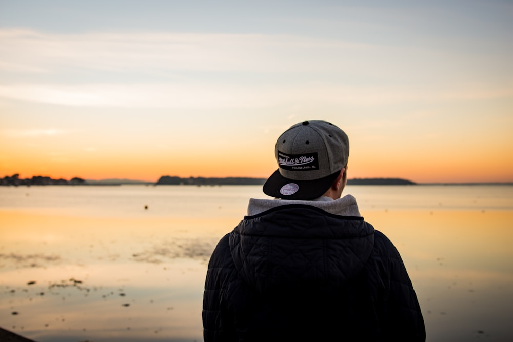 man wearing cap standing facing body of water