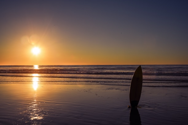 Sunset casting warm colors over a serene beach with surfboards and yoga mats.