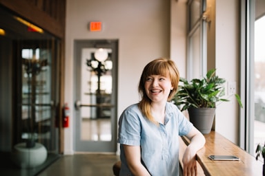 none,how to photograph smiling woman by a window; woman sitting in front of brown wooden table