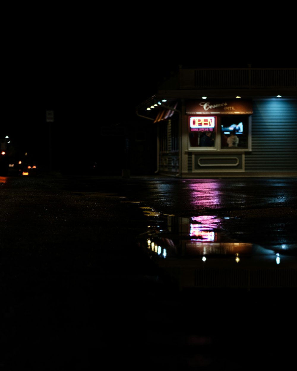 A store in the dark and a puddle reflecting the neon lights from the storefront window