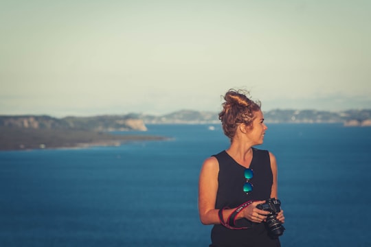 woman wearing black V-neck sleeveless dress holding DSLR camera in front of sea in Mount Victoria New Zealand