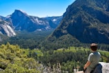 A thoughtful person sitting on a rock overlooking a mountain landscape.