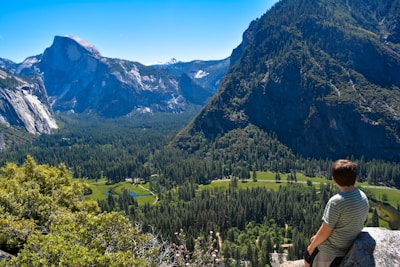 A thoughtful person sitting on a rock overlooking a mountain landscape.