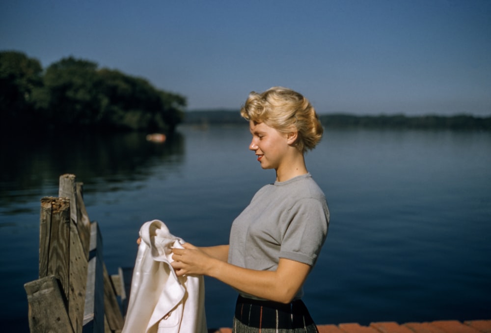 woman holding white textile standing beside body of water