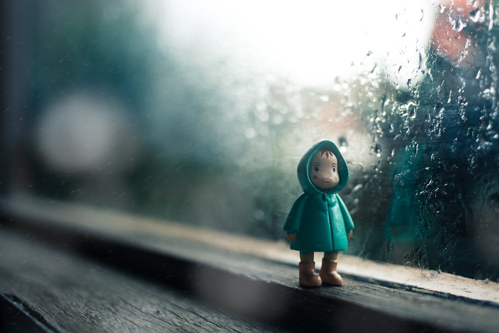 kid wearing green jacket mini figure beside glass window