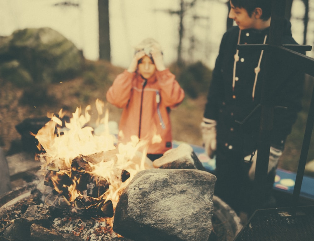 man in black sweatshirt standing in front of fire place surrounded by rocks during daytime