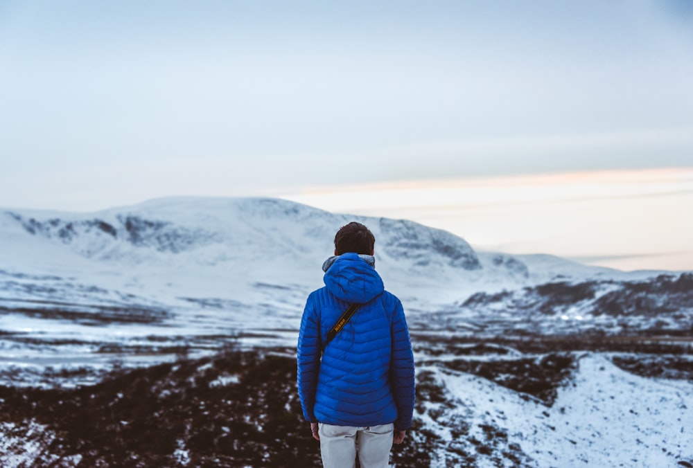 Person im blauen Kapuzenpullover mit Blick auf schneebedeckten Hügel