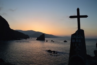 A peaceful sunrise over a quiet sea with a subtle cross silhouette in the background.