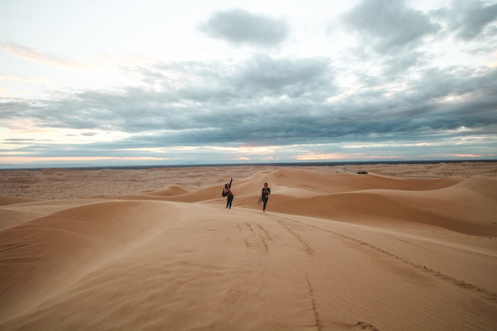 2 personas caminando en la playa de arena marrón durante el día