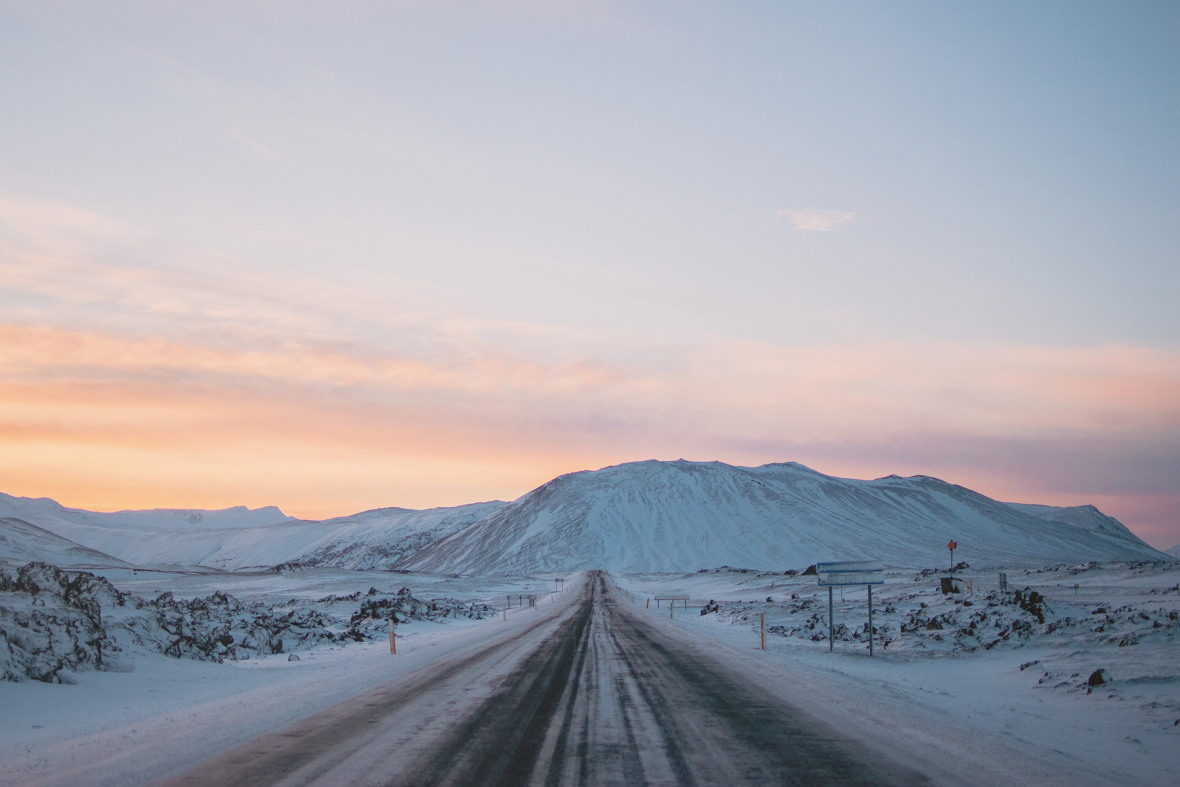 A snow-covered road through lava fields on the Snæfellsnes peninsula, the low winter sun tinting the sky pink