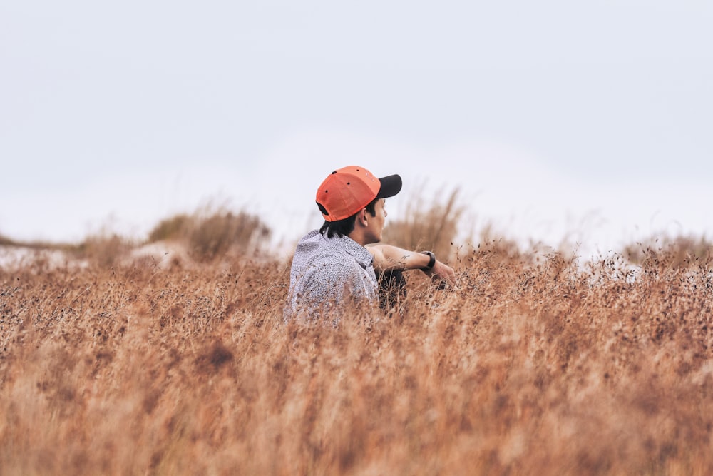 sitting man wearing red cap on brown flower field at daytime