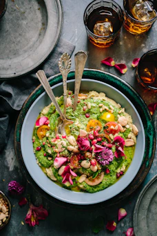 Hummus topped with green herb sauce, cherry tomatoes, pomegranate seeds, and edible flowers