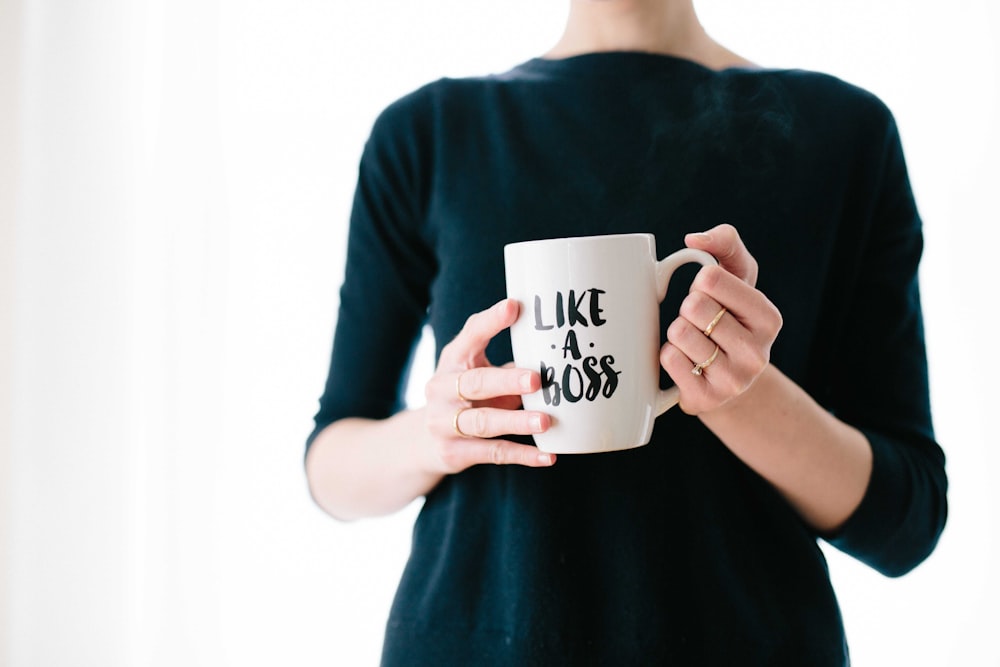 A woman holding a white mug with a âlike a bossâ print