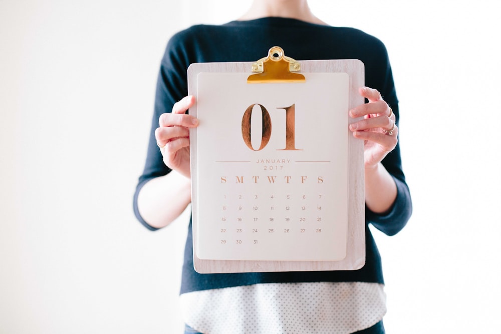 A woman holding up a clipboard with a calendar in front of her chest