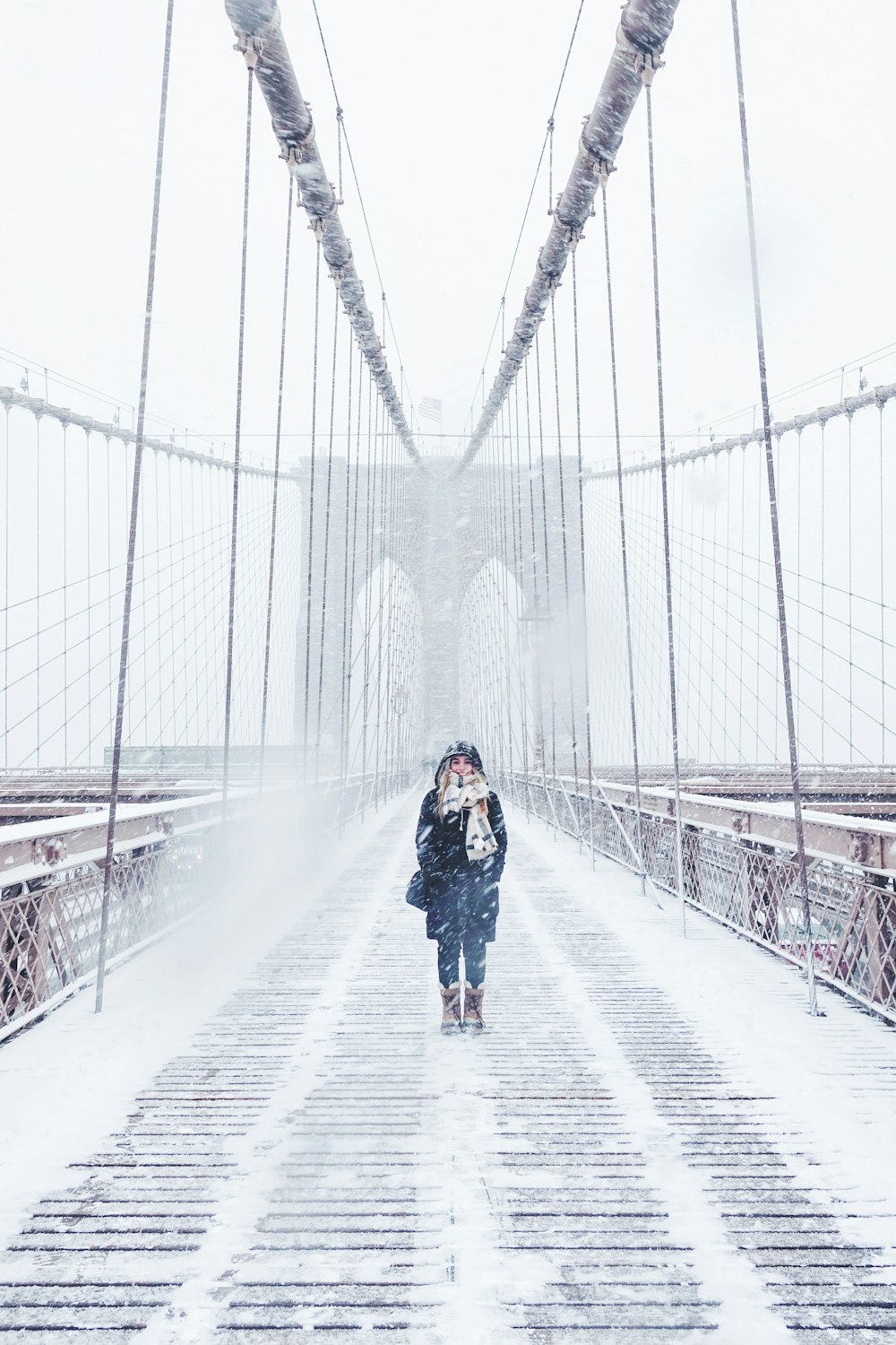 A woman walking across the Brooklyn Bridge in winter attire