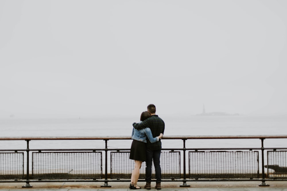 couple standing in front of fence near body of water