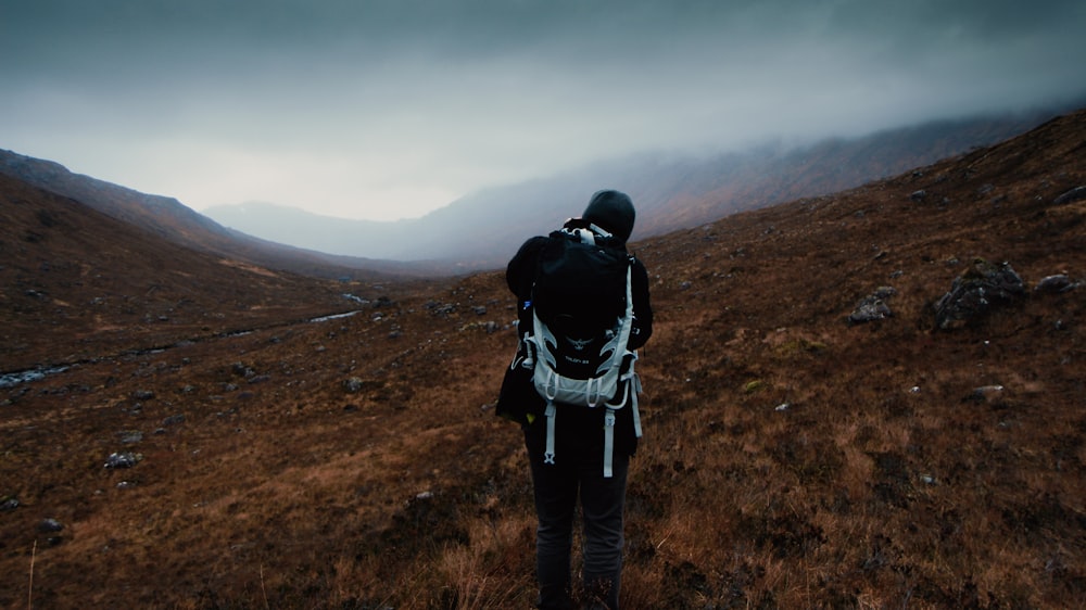 man carrying hiking bag standing under cloudy sky