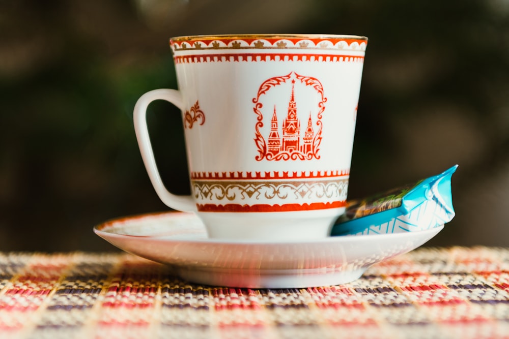 selective focus photography of white-and-red teacup on saucer with blue labeled food pack