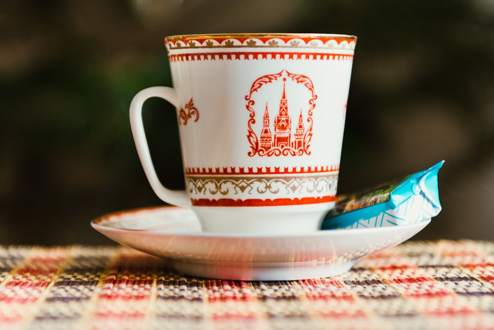 Fotografía de enfoque selectivo de taza de té blanca y roja en platillo con paquete de alimentos con etiqueta azul