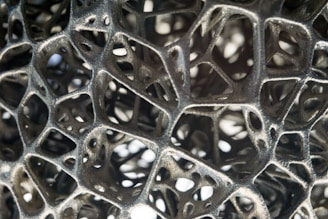 An intricate latticework of organic and abstract forms creates a complex network of interlinked structures. The design is metallic with a rough texture, evoking a sense of technological or natural complexity.