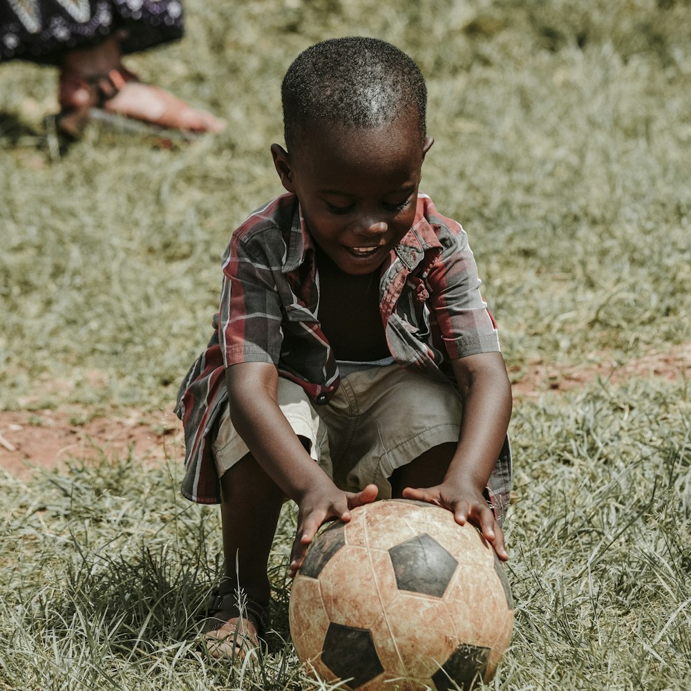 Niño sonriente sentado mientras sostiene la pelota de fútbol durante el día
