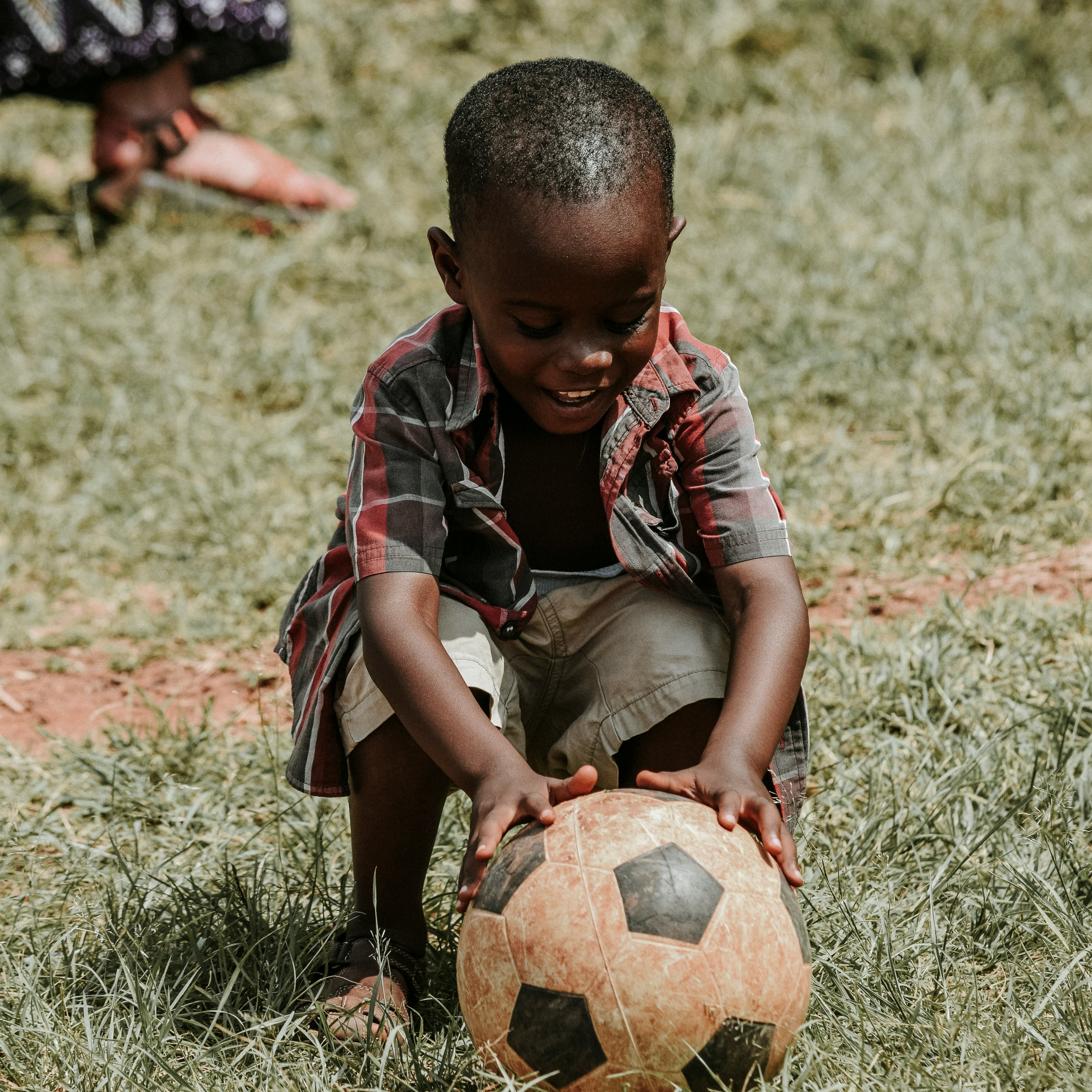 smiling boy sitting while holding soccer ball at daytime